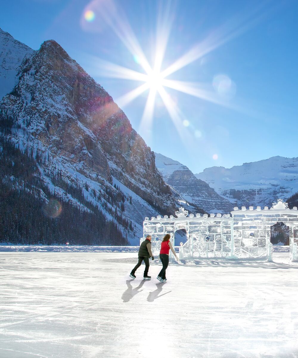 Two people skating on the ice rink on Lake Louise with an ice castle and glacier in the background